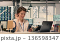 Smiling woman participating in video call from workstation in office, using smartphone for online meeting. Corporate video conference focused on strategy, KPI analytics and performance review. 136598347