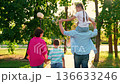 Happy parents, children, son mother, daughter father shoulders, walk together, enjoying sun nature. Family strolling in park, happy people. Family picnic with child in outdoors. Dad mom son traveling 136633246
