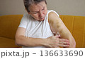 Older Woman Carefully Massaging Injured Arm, Elderly Lady Gently Applying Balm To Her Swollen Arm At Home, Senior Woman Uses Tender Massage Motions To Soothe Her Bruised Arm While Seated On Sofa 136633690