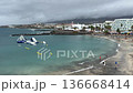 Aerial view of Tenerife beach bay with calm Atlantic water, black sand shoreline, seaside hotels and inflatable waterpark. Cloudy weather, travel vacation concept with copy space. 136668414