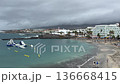 Aerial view of Tenerife beach bay with calm Atlantic water, black sand shoreline, seaside hotels and inflatable waterpark. Cloudy weather, travel vacation concept with copy space. 136668415