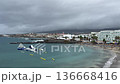 Aerial view of Tenerife beach bay with calm Atlantic water, black sand shoreline, seaside hotels and inflatable waterpark. Cloudy weather, travel vacation concept with copy space. 136668416
