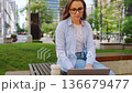 A woman sitting in the park with a laptop and working during the summer day 136679477