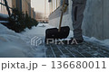 Maintenance Worker in Winter Clothing Shovels Snow From Paved Walkway Along Building Exterior 136680011