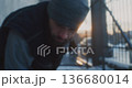 Bearded Man Wearing Beanie and Workwear Vest Performs Manual Snow Removal Near Modern Metal Fence 136680014