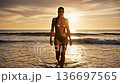 Beautiful confident woman in golden swimsuit walking from ocean at sunset 136697565