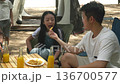 Family camping trip, kids enjoy outdoor fun, beach tent setup, relaxed children share snacks, man feeds girl tasty crisp, boy plays near tent, juice bottles await, sunny day adventure. 136700577