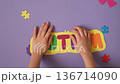 The child places a yellow card with multicolored letters forming the word autism on a background decorated with puzzle pieces 136714090