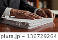 elderly black lawyer reviewing stacked documents on polished wooden desk closeup of wrinkled hands turning pages cufflinks visible serious study atmosphere bookshelf background 136729264