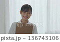 バインダーを抱えて微笑む白衣を着た若い女性（スローモーション） 136743106