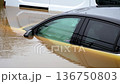 Submerged cars trapped in deep floodwater after torrential rainfall. Muddy river overflow surrounding vehicles and causing severe property damage. Extreme weather intensifying and disrupting transport 136750803