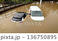UK flooding disaster leaving cars submerged in deep muddy water after heavy rain. Severe weather conditions turning rural road into flooded zone with stranded vehicles. Natural catastrophe causing 136750895