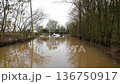 Severe flood turning rural road into deep muddy water with car submerged. Extreme weather aftermath leaving vehicle stranded in high water across countryside. Natural disaster scene with 136750917
