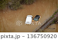 Aerial drone view over flooded road with cars sinking in muddy river. Heavy rain causing traffic disruption and vehicles submerging under brown water. Urban flooding disaster affecting transportation 136750920