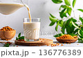 Plant milk mid pour into glass, frozen motion, grains and leaves on rustic surface 136776389