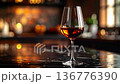 Close up of red wine glass on dark reflective surface, warm light and soft focus droplets 136776390