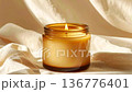 Glass candle with gold detail on fabric, gentle light, shallow focus on texture 136776401