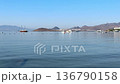 Wide-angle view of a calm, blue bay with yachts and sailboats anchored near a white hillside village. Distant mountains and a clear sky create a serene Mediterranean coastal landscape. High quality 4k 136790158