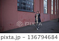 Woman walks with coffee near a building with large windows in the city during daytime 136794684