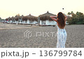 Woman walking on beach at sunset near thatched umbrellas and cabanas 136799784