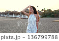 Close up side view of woman posing at sunset beach with umbrellas and cabanas 136799788