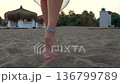 Woman bare feet walking on sandy beach at sunset with cabanas and umbrellas 136799789