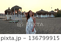 Woman posing on empty sandy beach at sunset with umbrellas and cabanas 136799915
