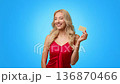 A woman with long blonde hair is smiling and winking while holding a credit card. She stands against a bright blue backdrop, conveying excitement and confidence. A woman with long blonde hair is smiling and winking while holding a credit card. She stands against a bright blue backdrop, conveying excitement and confidence. 136870466