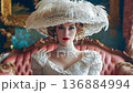 Elegant woman in vintage dress and feathered hat sitting on velvet sofa. 136884994