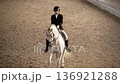 Female rider on white horse in indoor arena daytime top view 4K 136921288