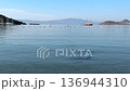 Panoramic view of a calm, blue bay with a wooden sailboat anchored in the center. Distant mountains and small islands sit under a clear sky with a string of buoys in the foreground. High quality 4k 136944310