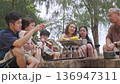 Family enjoys happy camp summer vacation moments, sharing picnic food and grilling fresh vegetables with children during travel for delicious outdoor meal. 136947311