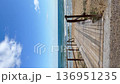 Wooden boardwalk leading to a quiet sandy beach with gentle waves and a blue sea. Sunlight casts creating a serene path to the ocean. Vertical video coastal relax and nature-inspired travel concepts 136951235