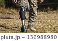 Military personnel walks confidently on grass with a prosthetic leg during a sunny afternoon outside 136988980