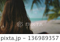 Young woman is standing on a white sand beach with turquoise water and palm trees, enjoying the tropical climate. She is breathing in the fresh air and feeling the warm sun on her skin 136989357