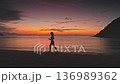 Silhouette of sporty woman running barefoot on the beach in Thailand, enjoying stunning sunset over calm sea with colorful sky and distant islands 136989362