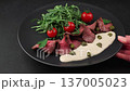 Vitello Tonnato with arugula, cherry tomatoes, capers, and parsley. A popular Italian appetizer made with veal and a tuna-anchovy sauce. The woman puts the plate on the table. Selective focus. 137005023