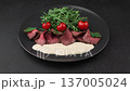 Vitello Tonnato with arugula, cherry tomatoes, capers, and parsley. A popular Italian appetizer made with veal and a tuna-anchovy sauce. The woman adds capers. Selective focus, black background. 137005024