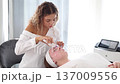 A professional skincare specialist applies a cooling gel on a client's face with a gentle spatula, focusing on precise treatment. 137009556