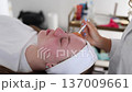 A beautician gently applies a face mask to a woman lying on a spa bed during a facial treatment. Calm atmosphere 137009661