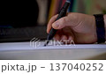 A person's hand writes with a black marker on paper on a table 137040252