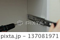 Man using a electric drill to attach a metal drawer slide to a piece of furniture during assembly. Furniture installation. 137081971