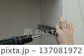 Man using a electric drill to attach a metal drawer slide to a piece of furniture during assembly. Furniture installation. 137081972