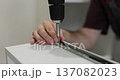 Close-up of person driving screw with cordless drill into furniture panel, assembling drawer. 137082023