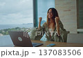 Happy woman celebrating success while working on laptop at home with ocean view. Remote work success and online business freedom concept showing real emotion, victory moment, modern digital lifestyle 137083506