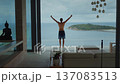 Success freedom concept with athletic man standing on luxury villa terrace facing ocean and island raising arms in victory pose. Success freedom success mindset and life achievement feeling  137083513