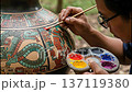 An artisan focuses on a Mayan ceramic piece. With careful attention, the artisan uses a brush to apply a fine red line on the vessel. This detailed work showcases cultural craftsmanship and skill. 137119380