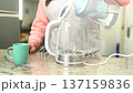 Young woman filling an electric glass kettle with water from a pitcher to prepare a hot beverage 137159836