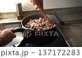 Male hands stirring diced beef with a wooden spatula in a hot non-stick frying pan on a cooktop 137172283