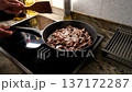 Chef stirring diced meat with a wooden spatula while frying in a pan on a modern cooktop 137172287